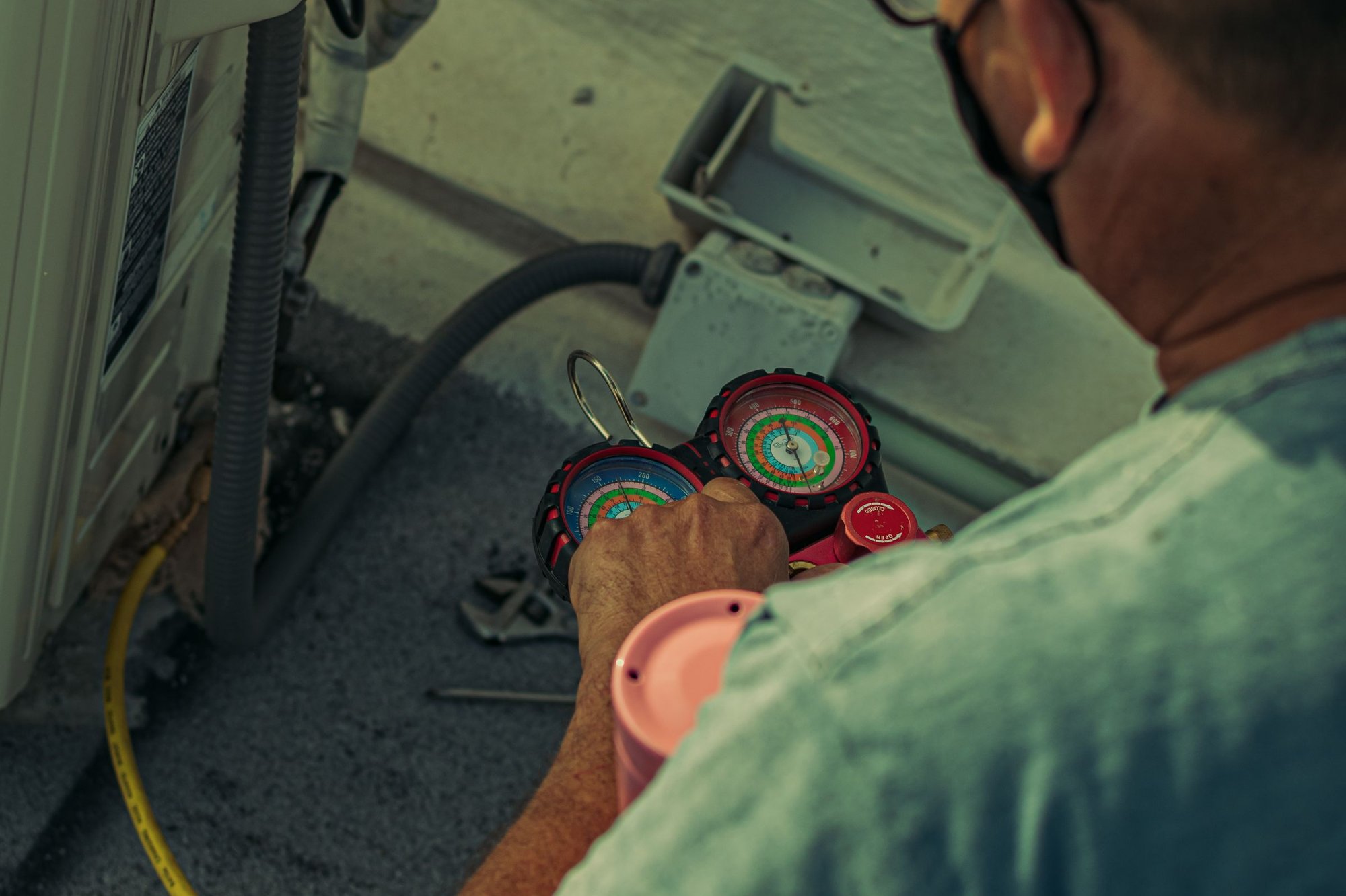 HVAC technician reading a refrigerant manifold gauge while servicing an outdoor AC unit