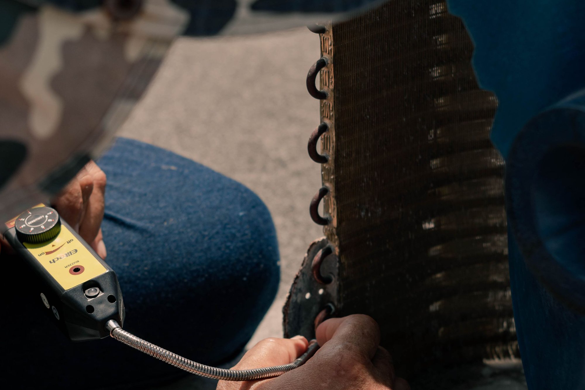 Technician checking an outdoor AC coil with a handheld leak detector