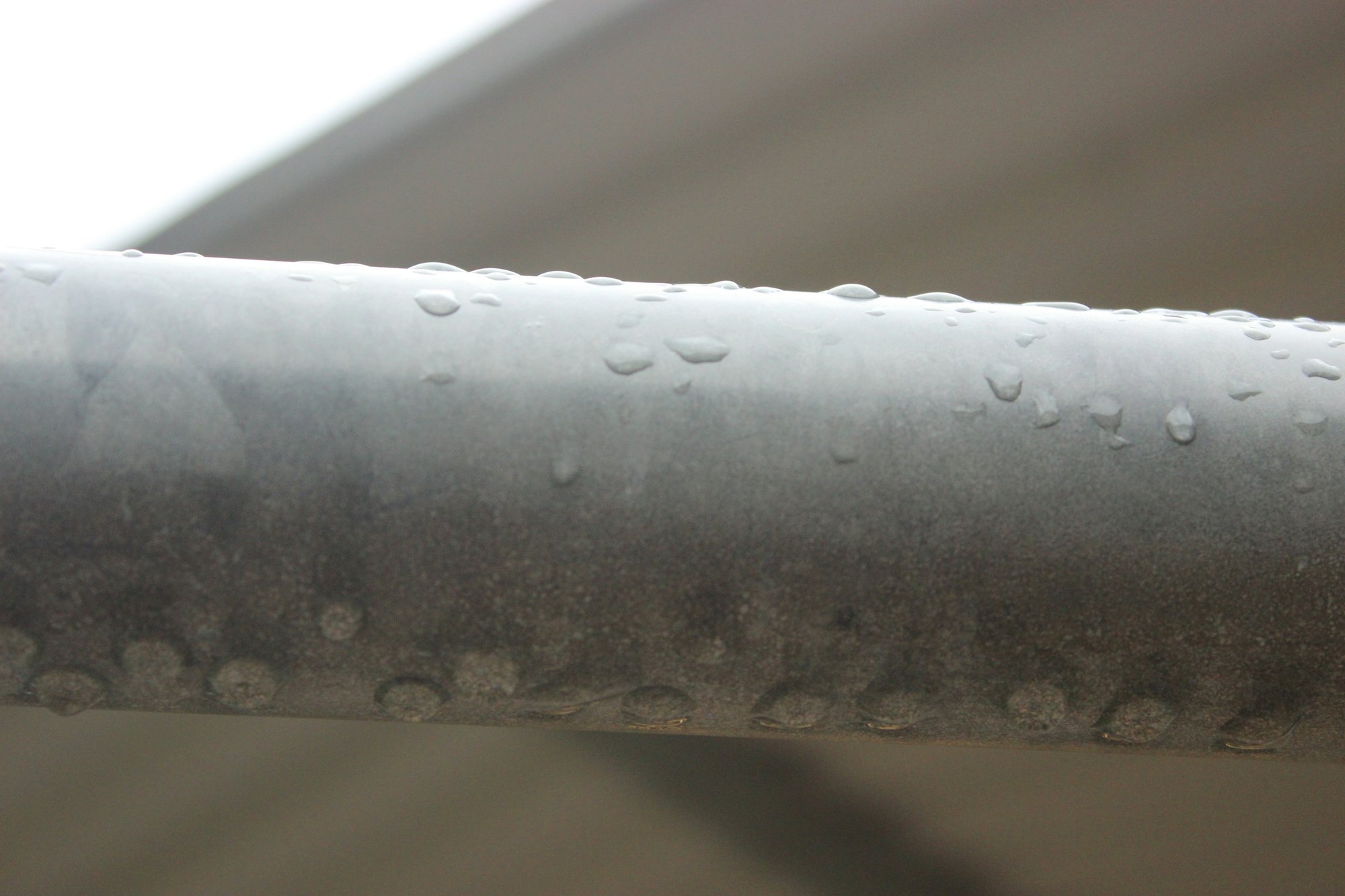 Water droplets beading on a metal pipe, like condensation on an air conditioner refrigerant line